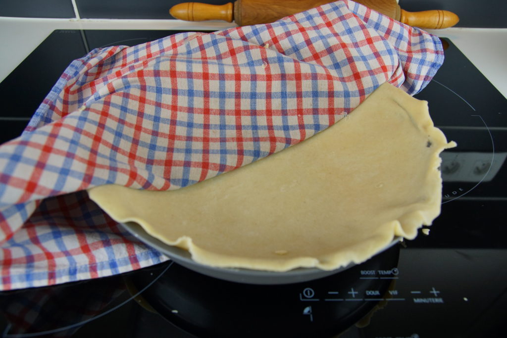 Pâte brisée dans le plat à tarte avec un torchon à carreaux